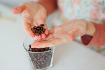 Close-up of girl's hands showing roasted coffee bean with blurred background behind. Shallow depth...