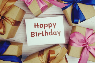 Happy Birthday text on paper card with gift box present on wooden background