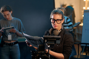Waist up portrait of female director looking at camera screen while leading video production on set