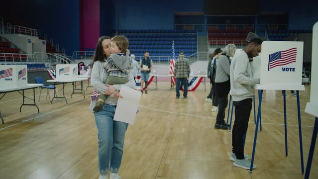 Woman with child on hands comes to voting booth. American citizens come to vote in polling station. Political races of US presidential candidates. National Election Day in United States. Dolly shot.