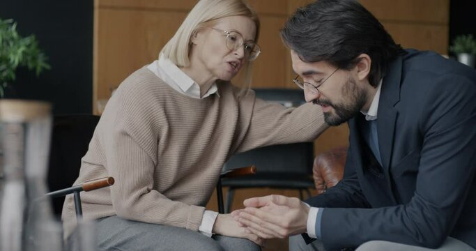 Middle Eastern businessman sharing negative emotion feeling sad while female therapist expressing support touching hand in office. Therapy and psychological support concept.