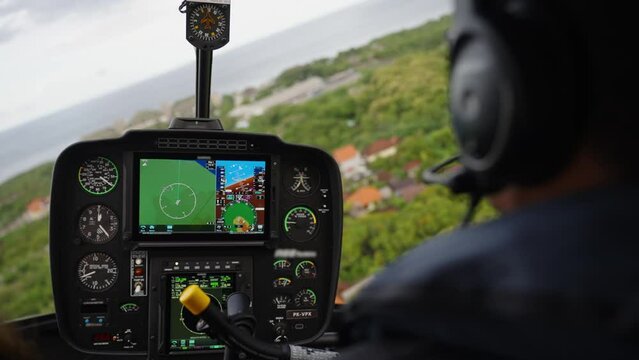 Helicopter flying, view from cabin behind the pilot. Aircraft cockpit. Dashboard with navigation and indicators. Flight above houses and trees 