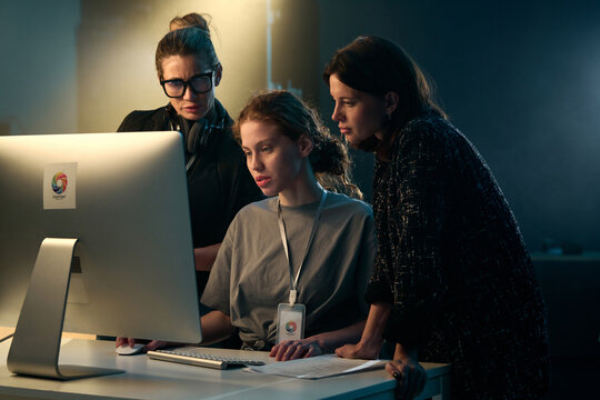 Minimal shot of three women looking at computer screen together on video production set with backlight