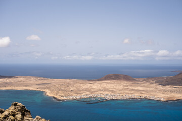 Fototapeta na wymiar Views of the island of La Graciosa from the viewpoint of El Rio. Turquoise ocean. Blue sky with big white clouds. Caleta de Sebo. Town. volcanoes. Lanzarote, Canary Islands, Spain