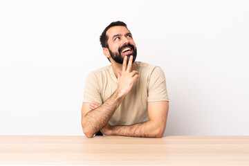 Caucasian man with beard in a table looking up while smiling.