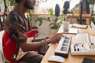 Cropped shot of young creative male composer with electric guitar and electronic synthesizer...