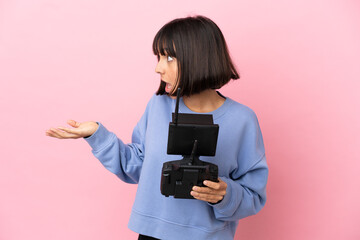 Young mixed race woman holding a drone remote control isolated on pink background with surprise...