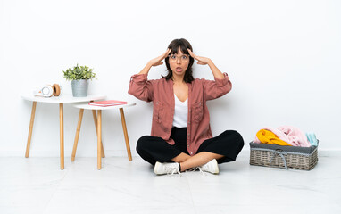 Young mixed race woman folding clothes sitting on the floor isolated on white background with surprise expression