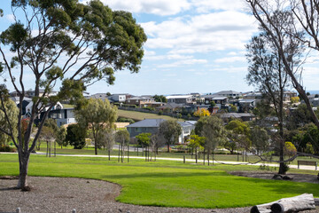 A public park features vast green open spaces, with sleek new suburban houses in the distance. Geelong VIC Australia. Concept of real estate development, housing market, property investment.
