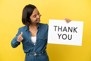 Young mixed race woman isolated on yellow background holding a placard with text THANK YOU with...