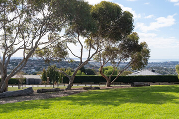 A public local park with green grassy outdoor space and trees, offering a skyline view of Geelong's suburban houses and neighborhoods. Wandana Heights Lookout, VIC, Australia.