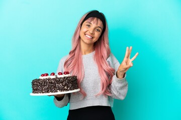 Young woman with pink hair holding birthday cake isolated on blue background happy and counting...