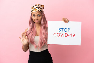 Young mixed race woman with pink hair isolated on pink background holding a placard with text Stop...