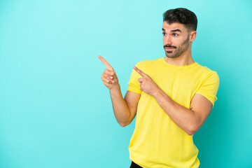 Young caucasian man isolated on blue background frightened and pointing to the side