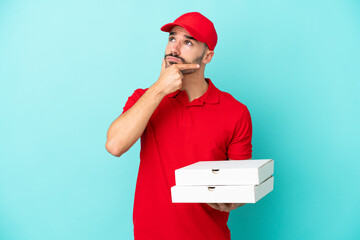 Delivery caucasian man picking up pizza boxes isolated on blue background having doubts