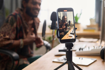 Smartphone on tripod with young creative composer or artist on screen carrying out livestream in...