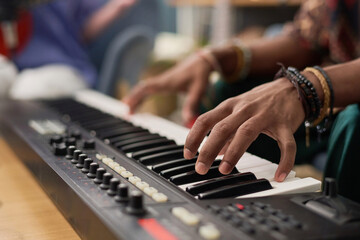 Hand of young unrecognizable male musician pressing keys of electronic synthesizer while composing,...