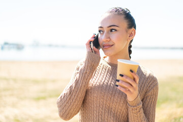 Young moroccan girl  at outdoors using mobile phone and holding a coffee