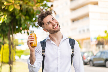 Young handsome man holding an orange juice at outdoors looking up while smiling