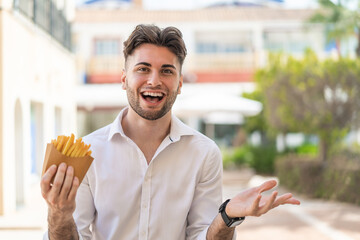 Young handsome man holding fried chips at outdoors with shocked facial expression