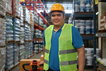 A Smiling man worker wearing a safety suite pulling a cart with a parcel box in a factory warehouse, a logistic industry concept
