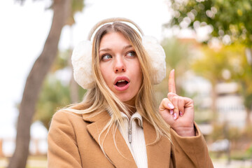 Young pretty blonde woman wearing winter muffs at outdoors thinking an idea pointing the finger up