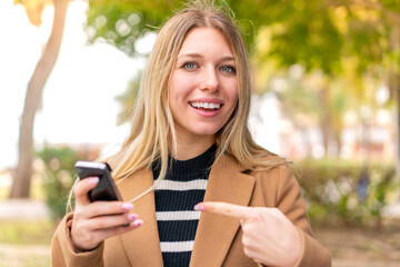 Young pretty blonde woman at outdoors using mobile phone and pointing it