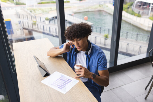A young biracial man wearing headphones, examining graphs on tablet