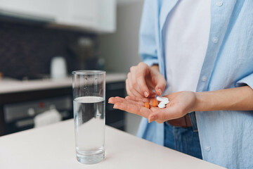 Woman holding pills and glass of water on kitchen countertop preparing medication in domestic setting