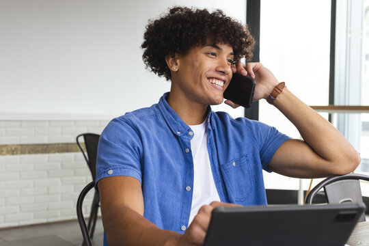 Young biracial man talking on phone, working on laptop at cafe in a modern business office - Powered by Adobe