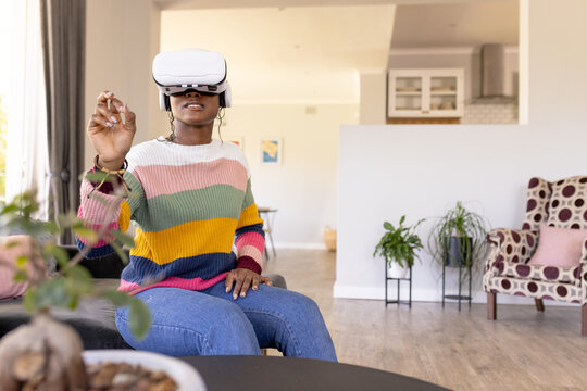 An African American young woman at home, wearing a virtual reality headset, reaching out at home, co