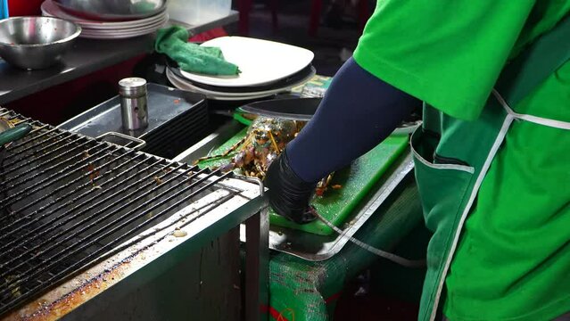 Asian chef slicing rainbow lobster with a knife at a street food market