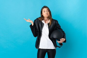Young Ireland woman holding a motorcycle helmet isolated on blue background having doubts while...
