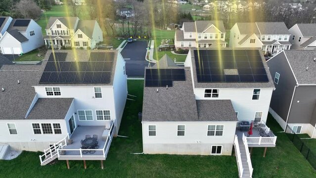 Animated golden sun rays shining on rooftop solar panels in modern American neighborhood. Renewable energy generation through photovoltaic array. Aerial truck shot.