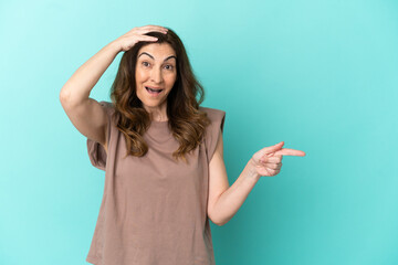 Middle aged caucasian woman isolated on blue background surprised and pointing finger to the side