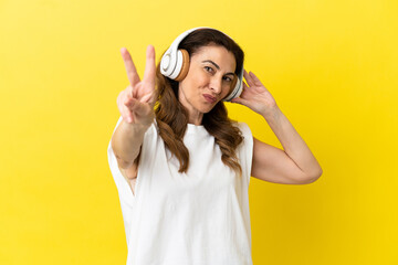 Middle aged caucasian woman isolated on yellow background listening music and singing