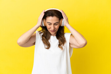 Middle aged caucasian woman isolated on yellow background listening music