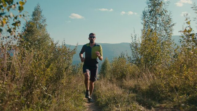 Focused sportive adult Caucasian male man guy runner sprinter jogging activewear running on trail training run cardio exercise fitness workout sport active lifestyle outdoors mountain landscape nature