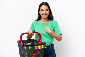 Young Colombian woman holding a shopping basket full of food isolated on white background with...