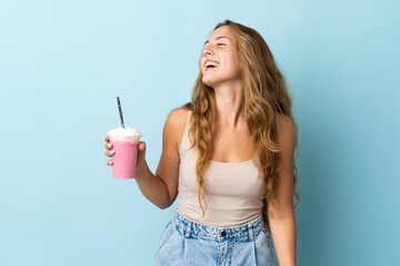 Young woman with strawberry milkshake isolated on blue background laughing
