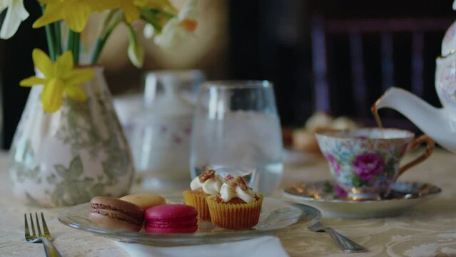 Elegant table is set with yellow daffodils and pink macrones and the tea is poured into the cup