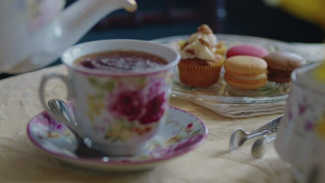 Rack focus from cup of tea to a plate of elegant pastries and french macrones