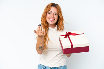 Young caucasian woman holding a gift iso0lated on white background inviting to come with hand. Happy that you came