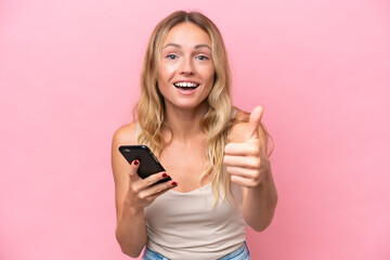 Young Russian woman isolated on pink background using mobile phone while doing thumbs up