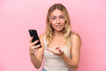Young Russian woman isolated on pink background using mobile phone and pointing it