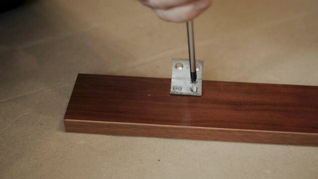 The phillips head of the screwdriver screws the self-tapping screw into the piece of furniture. Fastening the iron angle. Close-up