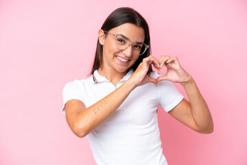 Young caucasian woman isolated on pink background With glasses making heart with hands