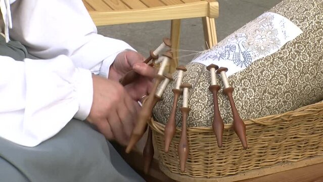 closeup of old woman making bobbin lace with her hands, detail shot of braiding thread