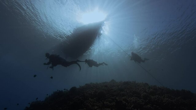 Backlight shot of scuba divers under a diving boat in clear blue water next to a tropical coral reef silhouette beauty shot at the island of Tahiti, French Polynesia