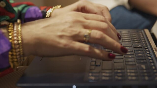 A close up of well adorned female hands typing on a laptop keyboard